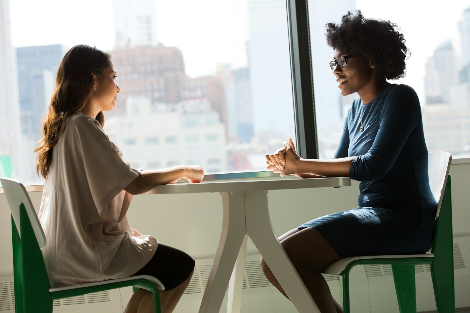 Zwei Frauen in einem Coaching- oder Beratungsgespräch an einem Tisch vor einem Fenster